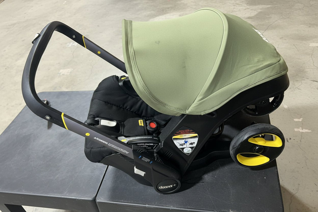 Green and black baby car seat with yellow wheels on a concrete floor.